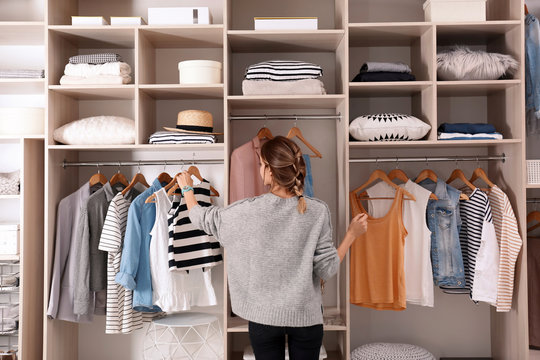 Woman choosing outfit from large wardrobe closet with stylish clothes and home stuff