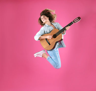 Young woman playing acoustic guitar on color background