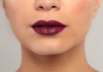 Young woman wearing dark lipstick on gray background, closeup