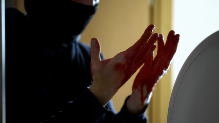 Shocked criminal looking at bloody palms, unintentional murder during robbery