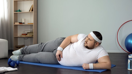 Chubby man lying on his back, watching and repeating online exercises, slimming