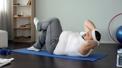 Persistent obese man pumping abdominal muscles doing twisting crunches, sport