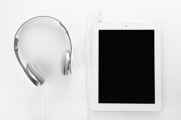 Tablet with blank screen and headphones on white background, top view