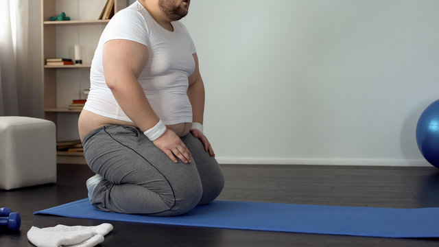 Fat man sitting on knees, resting after exhausted exercises, slimming process