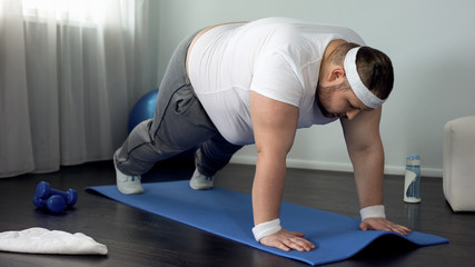 Fat male trying to do push up exercise at home, weak muscles, lack of motivation