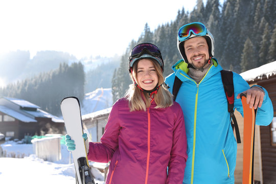 Happy couple with ski equipment spending winter vacation at mountain resort