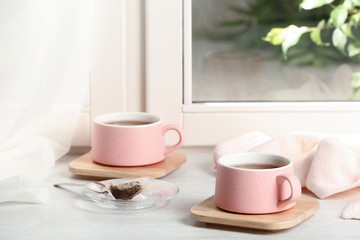 Cups of hot tea with wooden coasters on window sill