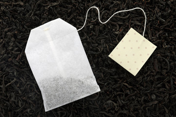 Unused tea bag with tag on dry leaves, top view. Space for text