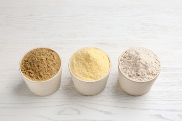 Bowls with different types of flour on white wooden background