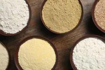 Bowls with different types of flour on wooden background, top view