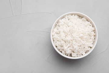 Bowl of boiled rice on color background, top view with space for text