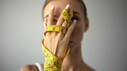 Anorexic model holding measuring tape, concept of harsh self-restriction in food - obrazy, fototapety, plakaty