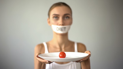 Thin girl with taped mouth holding plate with tomato, exhausting diet, anorexia
