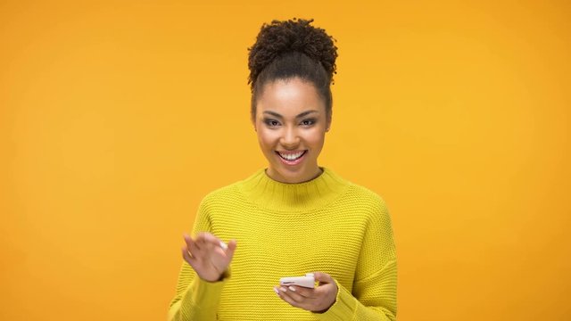 Smiling African-American woman chatting on smartphone and showing ok gesture