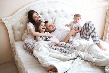  happy family is having fun together in bedroom. Family morning concept.   happy parents with two kids waking up in bed at home. 