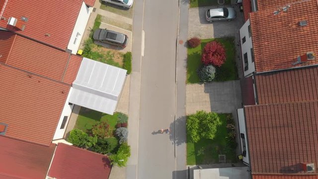 AERIAL TOP DOWN: Young runners living in the suburban neighborhood jog around the block on a sunny summer day. Healthy man and woman jogging down the empty street leading past middle class row houses.