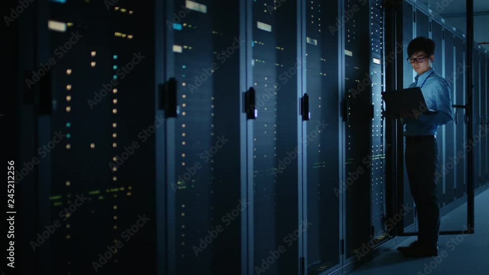 Leinwandbilder dark data center: male it specialist stands beside the row of operational server racks, uses laptop 