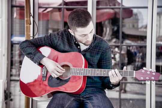 Handsome caucasian man playing the guitar outdoors on summer day in old european city. Rest, tourism, music concept.