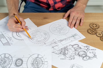 Man drawing gear wheel on paper using pencil