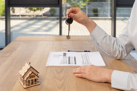 Cropped photo of woman hands with key and little house on table
