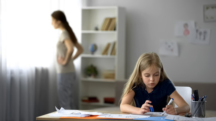Lonely child drawing picture, strict mother standing by window, tense atmosphere