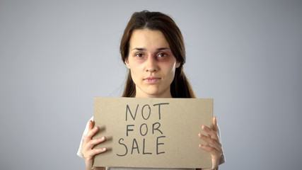 Bruised woman holding not for sale sign, human trafficking, sexual assault