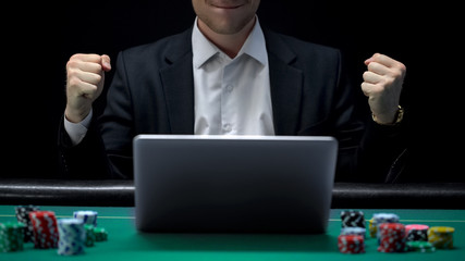 Gambler playing on laptop and showing success gesture, winning bet, fortune