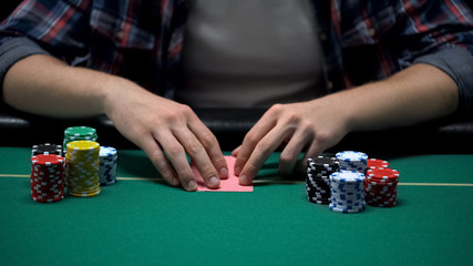 Young gambler ready to check his cards at casino poker game table, chance to win