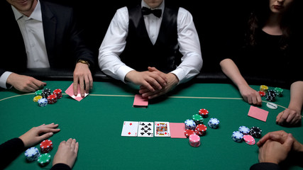 Upper class people at poker table checking card hands, casino entertainment