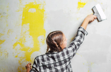 young teenager brunette girl with long hair applying white putty on a wall and smearing by putty...