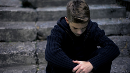 Sad teen sitting on old cracked steps, feeling grief and sorrow, parents loss