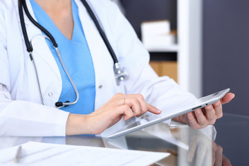 Woman doctor using tablet computer while sitting at the desk  in hospital office, closeup. Healthcare, insurance and medicine concept