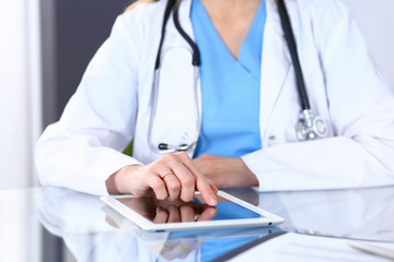 Woman doctor using tablet computer while sitting at the desk  in hospital office, closeup. Healthcare, insurance and medicine concept