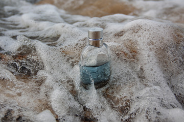 Perfume bottle in sea foam at the water's edge