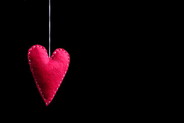 Red heart made of felt on a rope. Handmade isolate on black background.