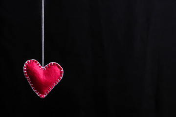 Red heart made of felt on a rope. Handmade isolate on black background.