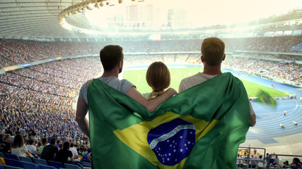 Football fans with Brazilian flag jumping at stadium, cheering for national team