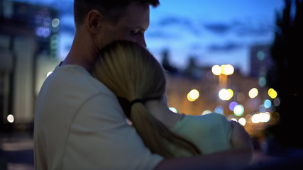 Girl leans on guy shoulder, hugging, looking at night city, closeness, safety