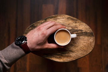 Man holding a cup of coffee on a wooden, vintage background. Hand of young businessman holding a mug of coffee. Vintage tones.  - 245218480
