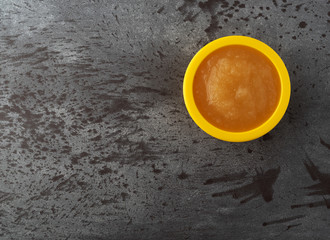 Top view of a small yellow bowl filled with applesauce offset on a gray background.