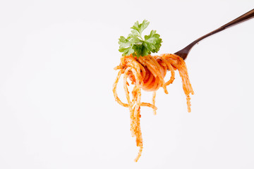 Spaghetti with pesto rosso on a fork decorated with parsley on a white background