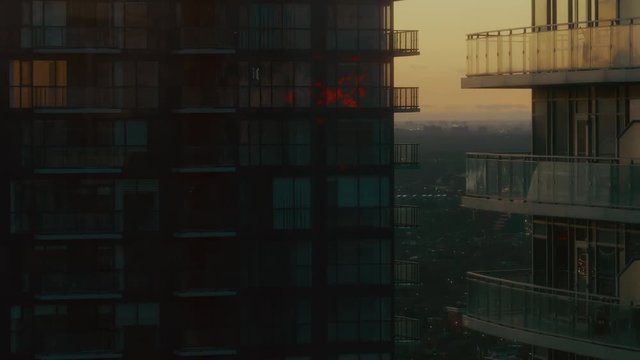Two high-rise condo buildings framing the distant city at sunset. The apartments are dark and moody. The image is quiet and peaceful. 