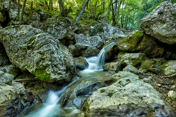 Beautiful waterfall in autumn forest in crimean mountains. Stones with moss in the water. Blurred water.