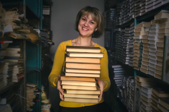 Happy Smiling Librarian Woman Holding In Hands A Stack Of Books In The Library. Exam Preparation.