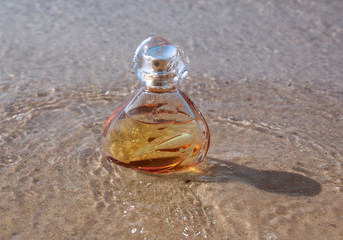 A bottle of perfume washed by the waves stands on the sand
