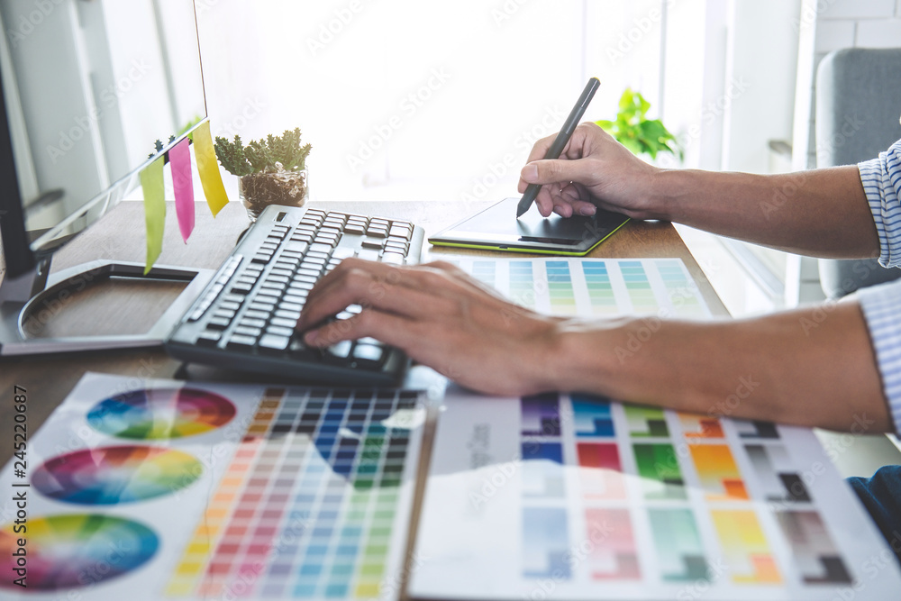 Poster Image of male creative graphic designer working on color selection and drawing on graphics tablet at workplace with work tools and accessories in workspace