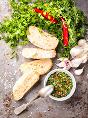  Argentinian green Chimichurri with ingredients.Raw homemade with ciabatta.Salsa or sauce made of parsley, garlic, oregano, hot pepper, olive oil, vinegar.Food Concept. Top View.