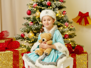 Little girl in the snow maiden costume with a teddy bear near th