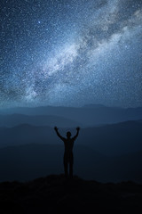 Night sky with stars and silhouette of a standing man with hands up achieving the top. Landscape with Milky Way. Milky Way at mountains
