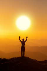Man silhouette standing with hands up achieving the top. Hiker welcomes a sun. Tourist open arms on sunrise mountain top